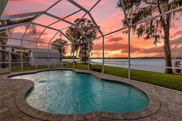 pool at dusk featuring a water view, a patio, a lanai, and a lawn