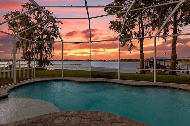 pool at dusk featuring a yard, a water view, and glass enclosure