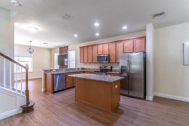 kitchen with hardwood / wood-style floors, a center island, appliances with stainless steel finishes, and decorative light fixtures