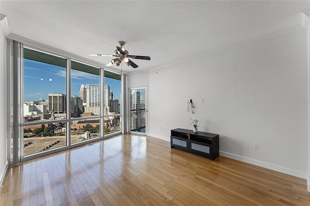 spare room featuring crown molding, wood-type flooring, a wall of windows, and ceiling fan