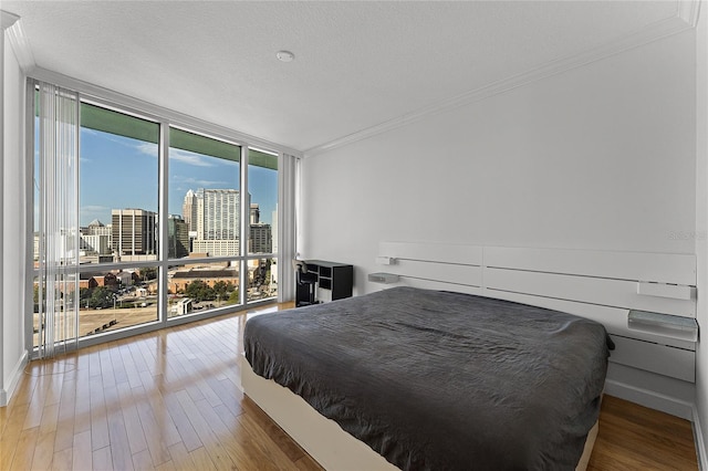 bedroom with expansive windows, a textured ceiling, wood-type flooring, and crown molding