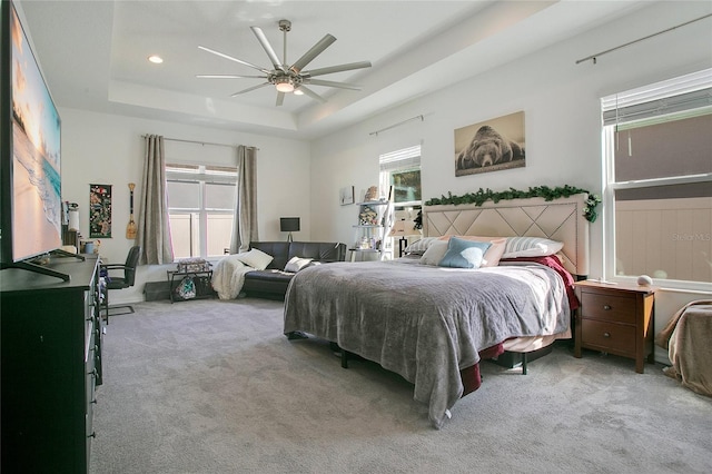 carpeted bedroom featuring ceiling fan, a raised ceiling, and multiple windows