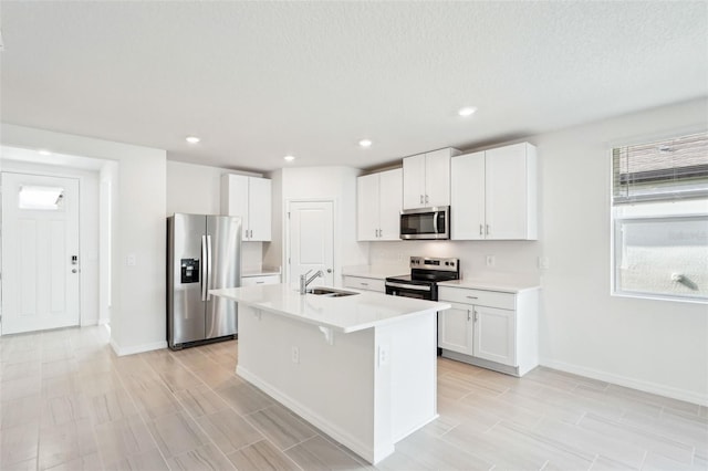 kitchen featuring sink, stainless steel appliances, a textured ceiling, a kitchen island with sink, and white cabinets