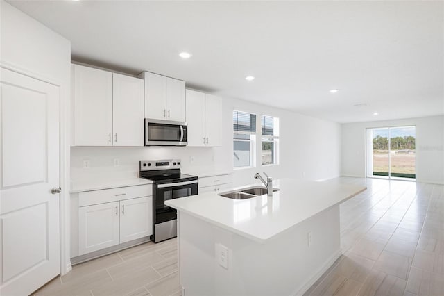 kitchen with appliances with stainless steel finishes, an island with sink, white cabinetry, and sink