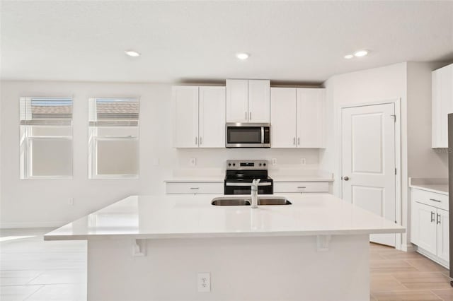 kitchen with white cabinets, a breakfast bar, an island with sink, and appliances with stainless steel finishes