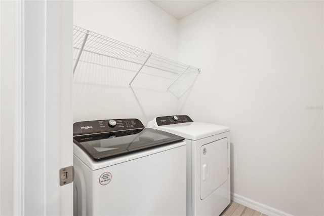 clothes washing area with washing machine and clothes dryer and light wood-type flooring