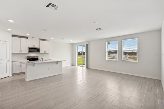 kitchen featuring stainless steel appliances, a kitchen island with sink, plenty of natural light, and white cabinetry