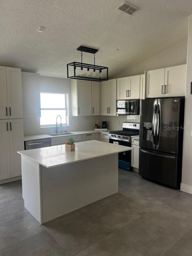 kitchen with white cabinets, appliances with stainless steel finishes, vaulted ceiling, sink, and a center island