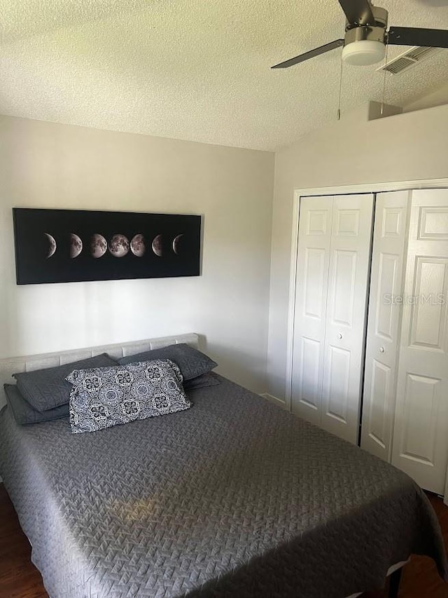 bedroom with a textured ceiling, dark hardwood / wood-style flooring, a closet, ceiling fan, and vaulted ceiling