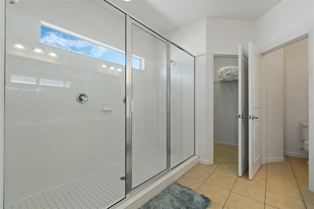 bathroom with a shower with door, toilet, and tile patterned flooring