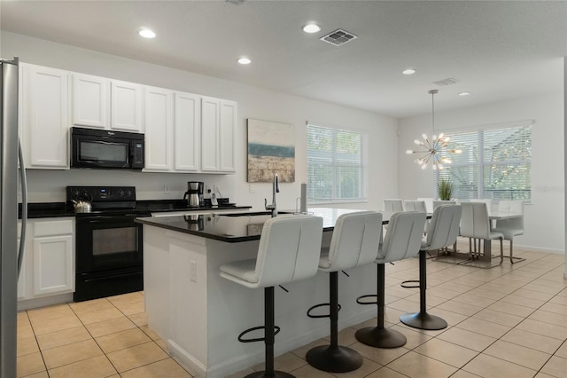 kitchen featuring white cabinets, hanging light fixtures, a breakfast bar area, a kitchen island with sink, and black appliances