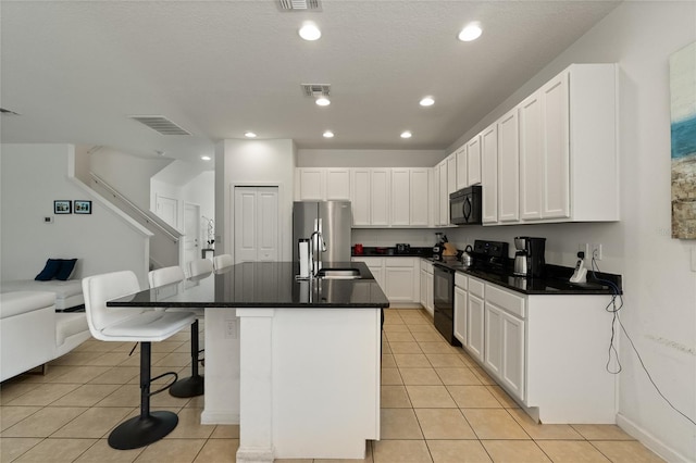 kitchen with white cabinets, light tile patterned floors, a kitchen breakfast bar, a kitchen island with sink, and black appliances