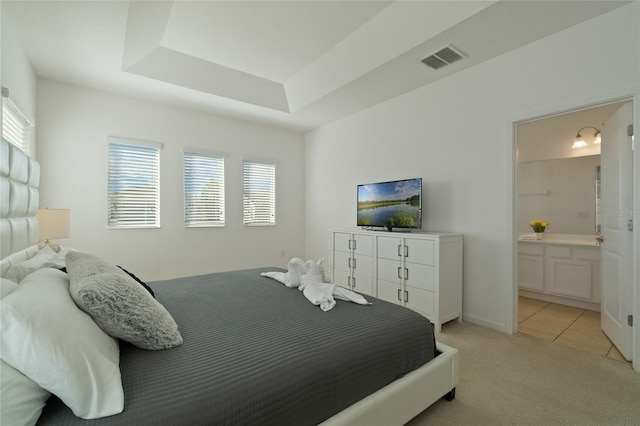 carpeted bedroom with ensuite bath and a raised ceiling