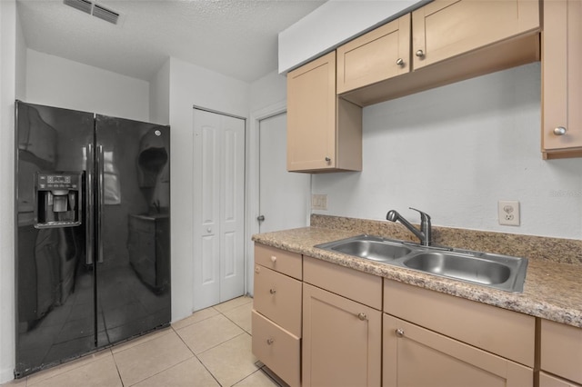 kitchen featuring light brown cabinetry, sink, a textured ceiling, black refrigerator with ice dispenser, and light tile patterned floors