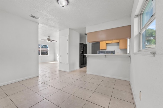 kitchen with black refrigerator with ice dispenser, kitchen peninsula, a kitchen breakfast bar, light tile patterned floors, and light brown cabinets