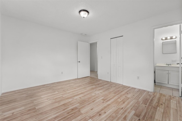 unfurnished bedroom featuring sink, a closet, ensuite bathroom, and light hardwood / wood-style floors