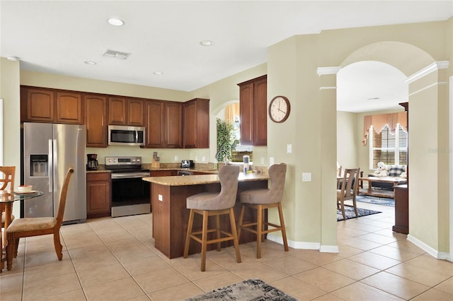 kitchen with appliances with stainless steel finishes, kitchen peninsula, light tile patterned flooring, and a kitchen bar