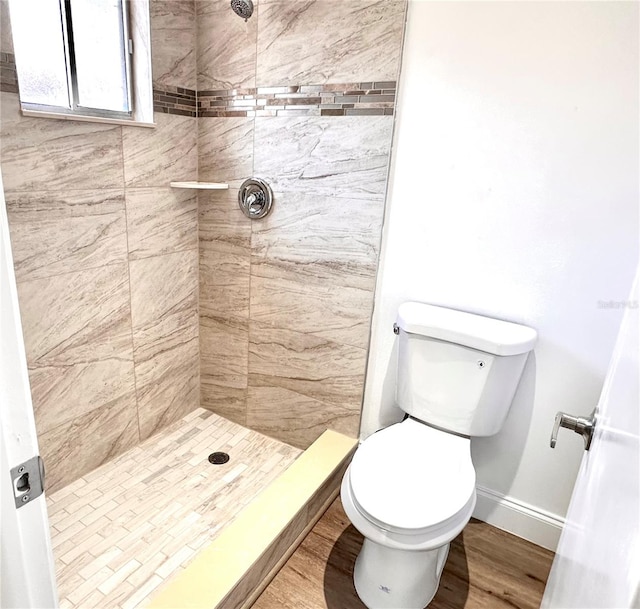 bathroom with hardwood / wood-style flooring, toilet, and a tile shower