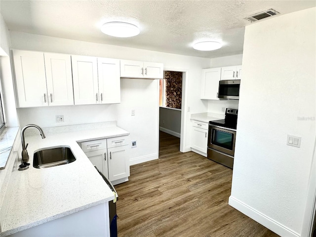 kitchen featuring stainless steel appliances, white cabinetry, sink, light stone counters, and dark hardwood / wood-style floors