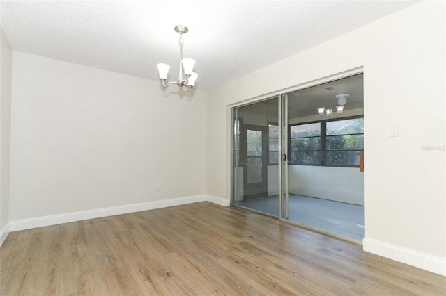 unfurnished room featuring baseboards, a notable chandelier, wood finished floors, and a textured ceiling