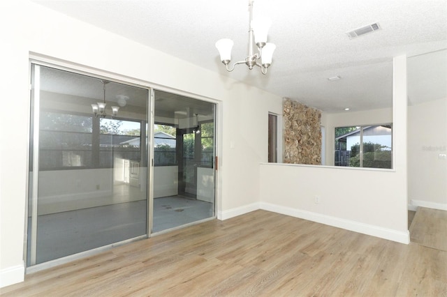 empty room with baseboards, a textured ceiling, visible vents, a notable chandelier, and wood finished floors
