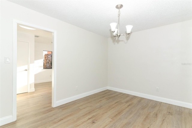 spare room featuring baseboards, light wood-type flooring, a textured ceiling, and a chandelier