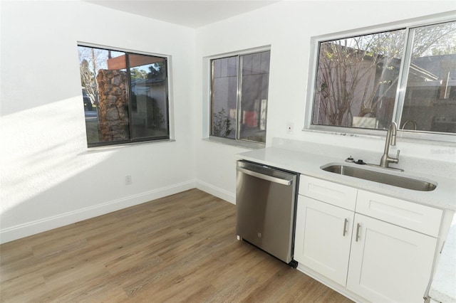 kitchen with white cabinets, light wood-style flooring, dishwasher, baseboards, and a sink