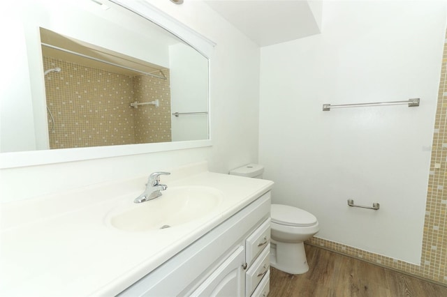 bathroom with toilet, vanity, wood finished floors, walk in shower, and baseboards