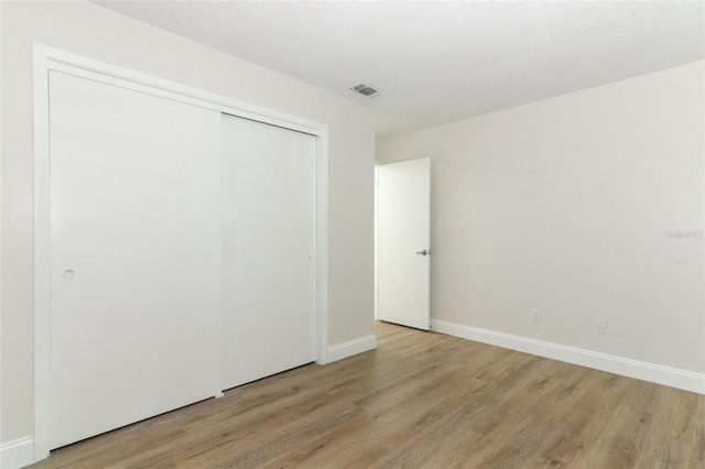 unfurnished bedroom featuring a closet, a textured ceiling, visible vents, baseboards, and light wood-style floors