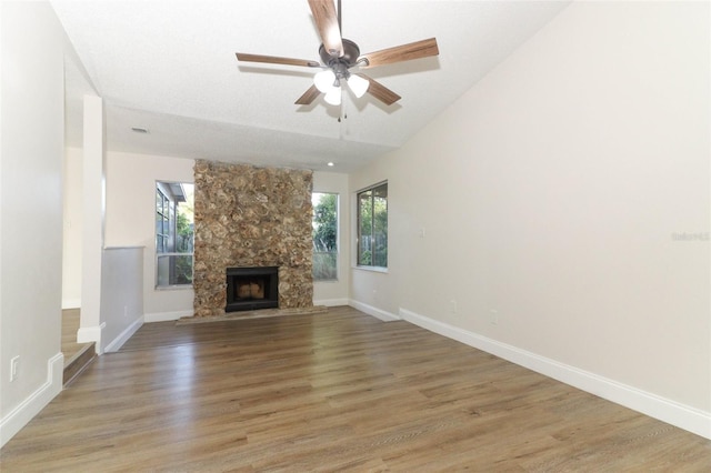 unfurnished living room with light wood finished floors, baseboards, a large fireplace, and a ceiling fan