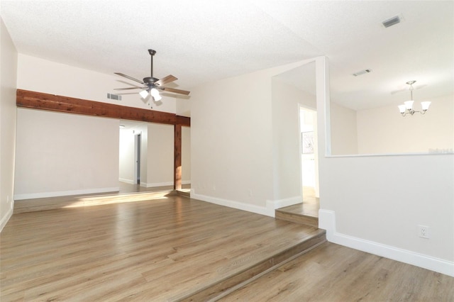 spare room with ceiling fan with notable chandelier, visible vents, baseboards, and light wood-type flooring