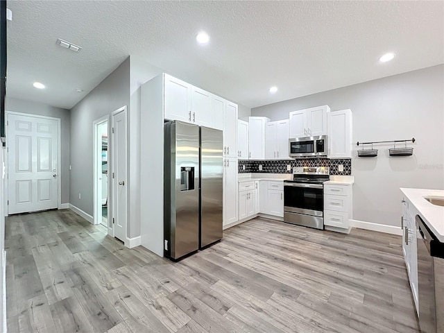 kitchen with backsplash, white cabinets, stainless steel appliances, and light wood-type flooring