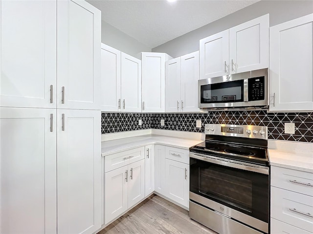 kitchen featuring backsplash, a textured ceiling, stainless steel appliances, white cabinets, and light hardwood / wood-style floors