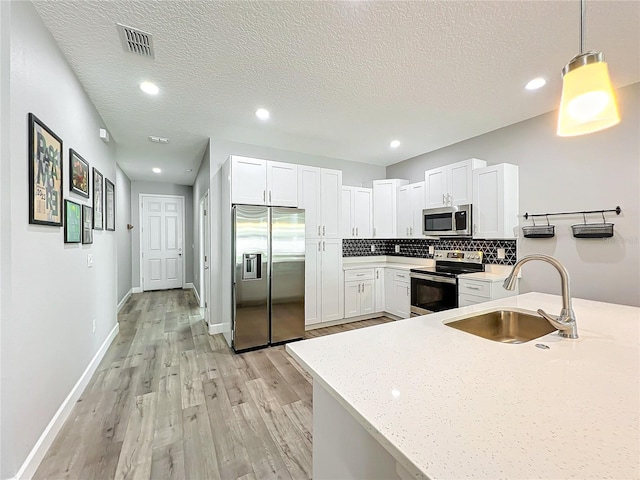 kitchen featuring pendant lighting, sink, light stone countertops, white cabinetry, and stainless steel appliances