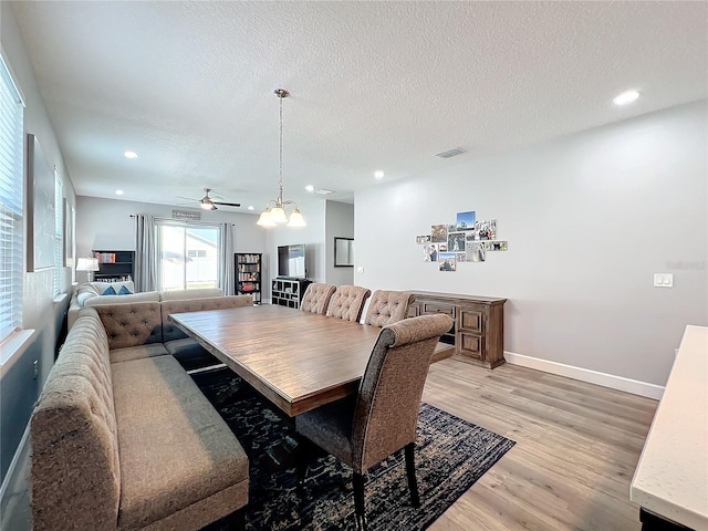 dining space featuring ceiling fan with notable chandelier, light wood-type flooring, and a textured ceiling