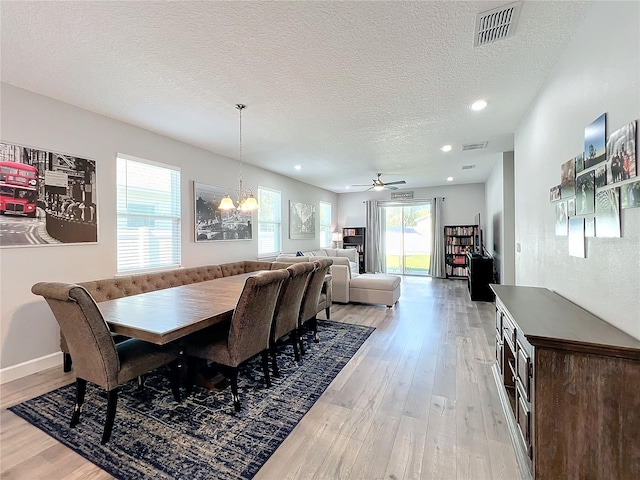 dining space with ceiling fan with notable chandelier, a textured ceiling, and light hardwood / wood-style flooring