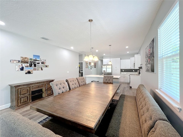 dining space with light hardwood / wood-style floors, sink, a textured ceiling, and an inviting chandelier