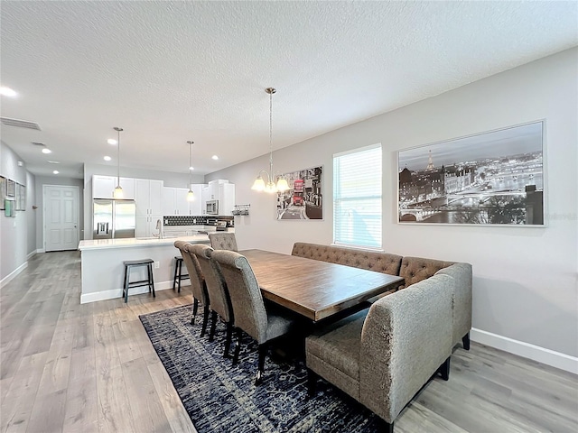 dining space featuring a notable chandelier, sink, a textured ceiling, and light hardwood / wood-style flooring