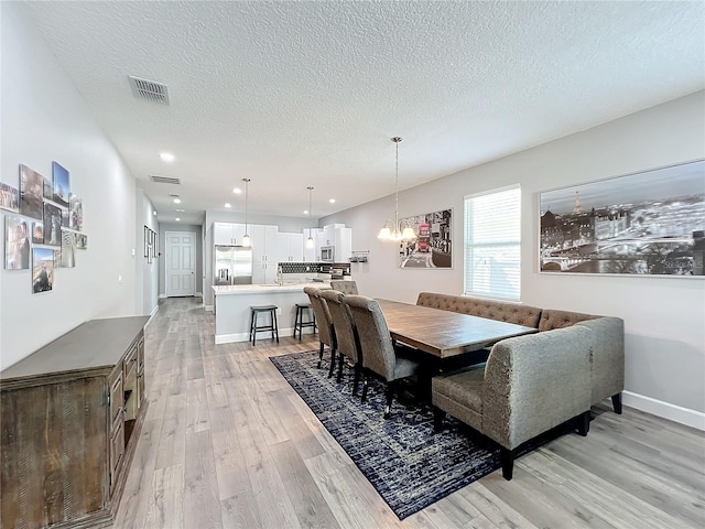 dining room with light hardwood / wood-style floors, a textured ceiling, and a notable chandelier