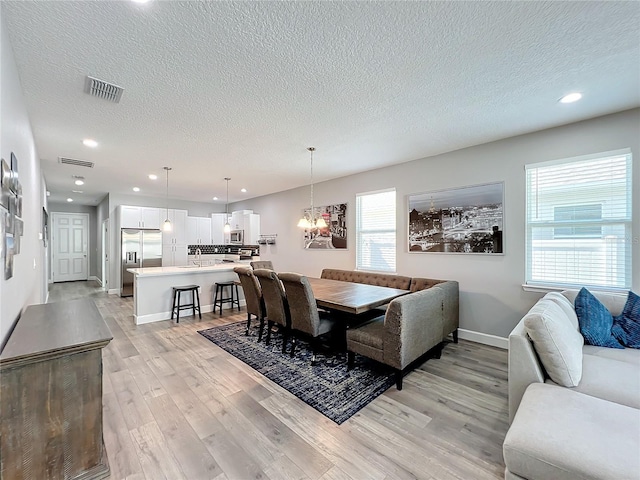 dining room with sink, light hardwood / wood-style flooring, a textured ceiling, and an inviting chandelier