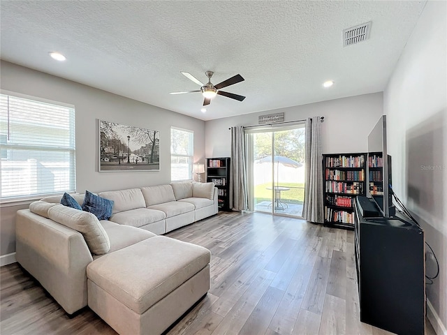 living room with ceiling fan, light hardwood / wood-style flooring, and a textured ceiling