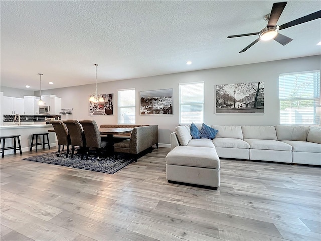 living room featuring ceiling fan with notable chandelier, light hardwood / wood-style floors, and a textured ceiling