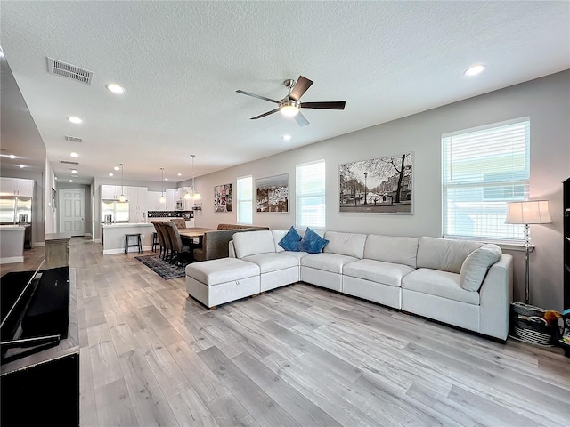 living room with ceiling fan, light hardwood / wood-style floors, and a textured ceiling