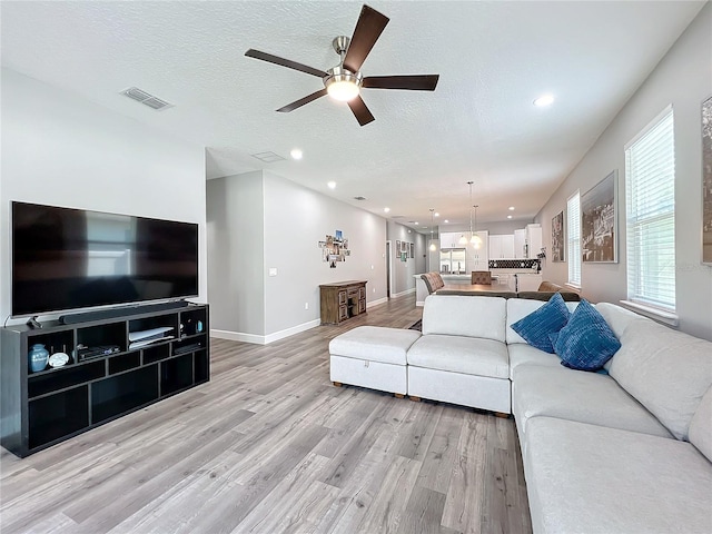 living room with a textured ceiling, light wood-type flooring, and ceiling fan