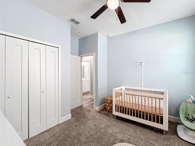 carpeted bedroom with a textured ceiling, a nursery area, a closet, and ceiling fan