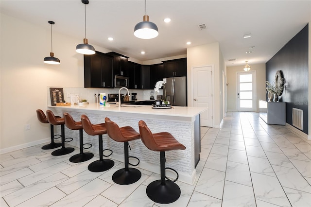 kitchen with kitchen peninsula, backsplash, appliances with stainless steel finishes, a kitchen breakfast bar, and sink