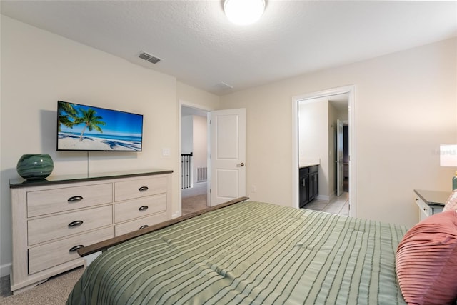 carpeted bedroom featuring ensuite bathroom and a textured ceiling