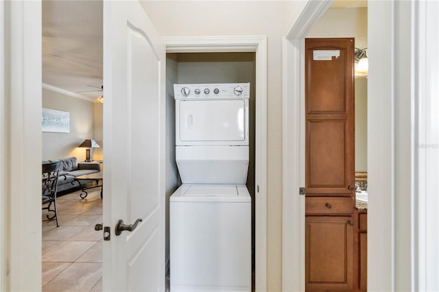 laundry room with crown molding, light tile patterned flooring, stacked washer and clothes dryer, and ceiling fan