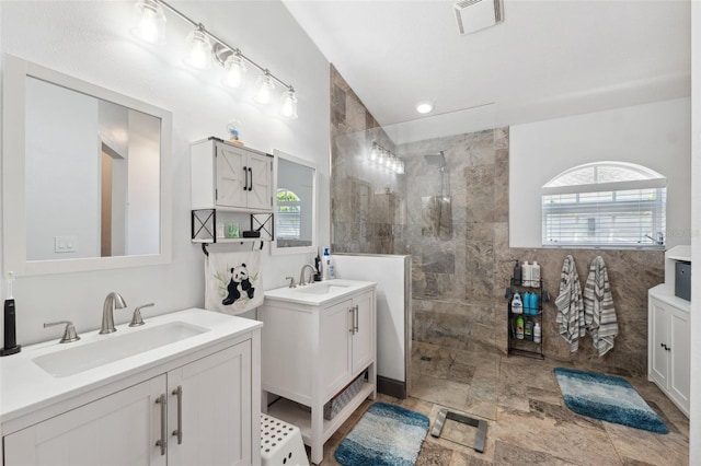 full bathroom with a walk in shower, two vanities, stone finish floor, and a sink