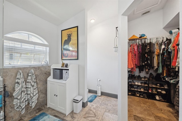 interior space with a shower, stone finish flooring, visible vents, vaulted ceiling, and a spacious closet